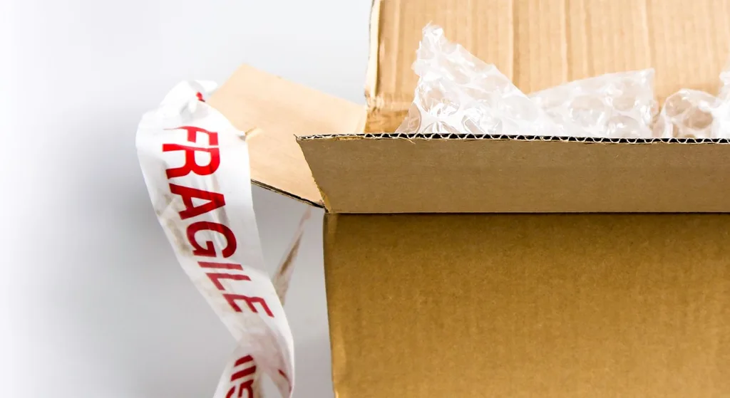 Open cardboard box with fragile sticker and bubble wrap on a white surface
